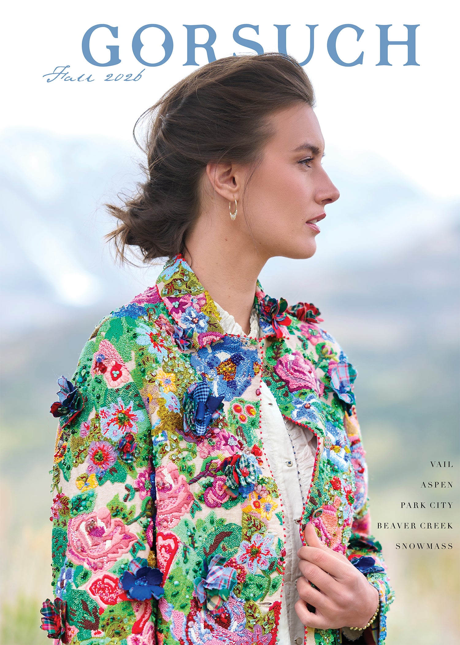 A woman in profile wearing a vibrant, heavily embellished floral jacket with 3D floral appliqués, set against a soft-focus outdoor mountain background. The brand name 'GORSUCH' is printed in blue at the top, and 'Fall 2026' is written in script.
