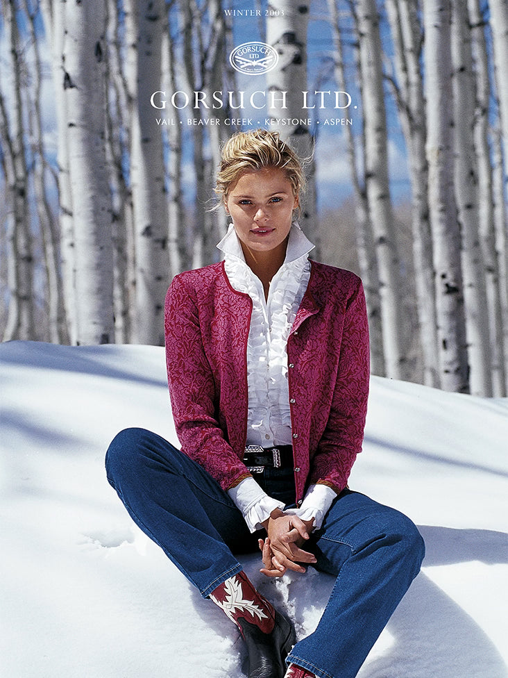 2003 Gorsuch catalog cover with women in white ruffled shirt and pink cardigan sitting in the snow with aspen trees in the background.