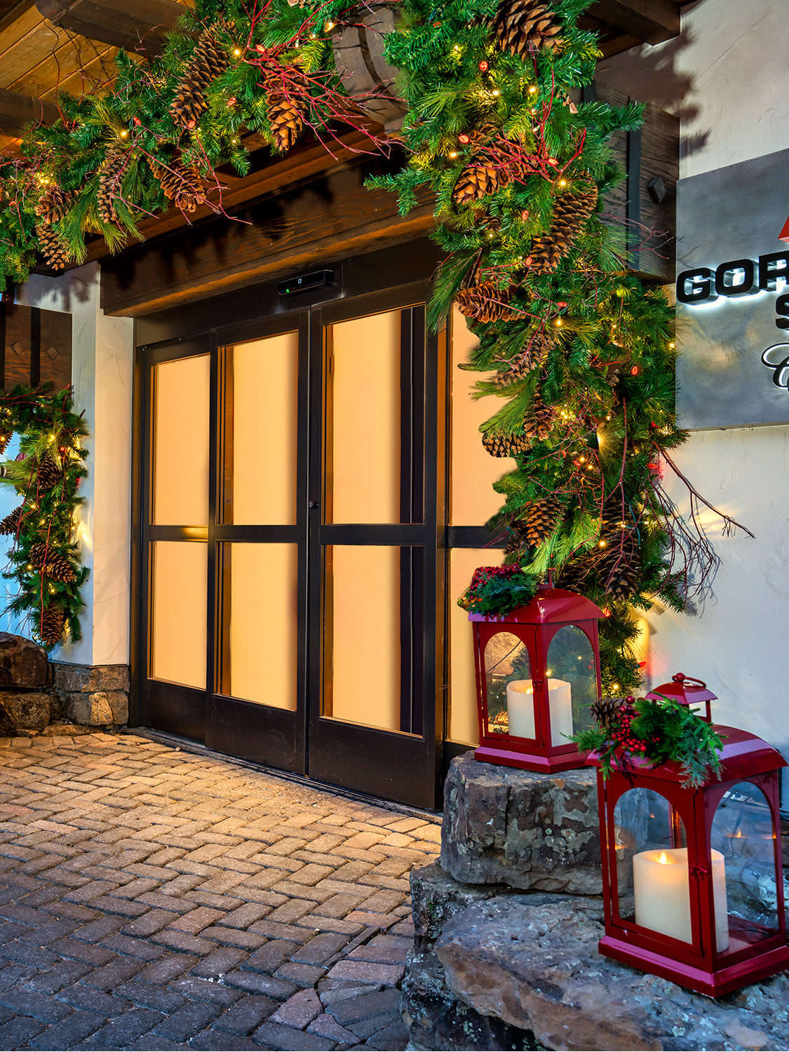 storefront of Gorsuch Ski Cafe in Vail with branded sign and garland with pinecones and red lanterns decorated for the holiday season.
