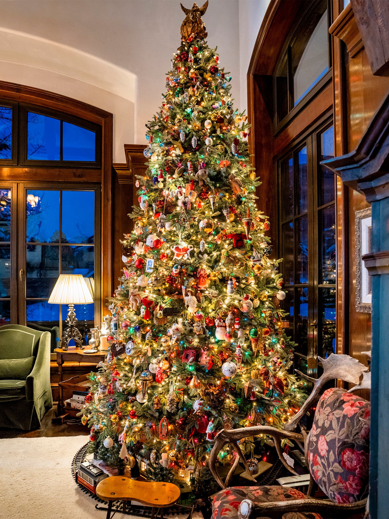 Large Christmas tree decorated with colorful ornaments and lights, with a toy train set beneath it.