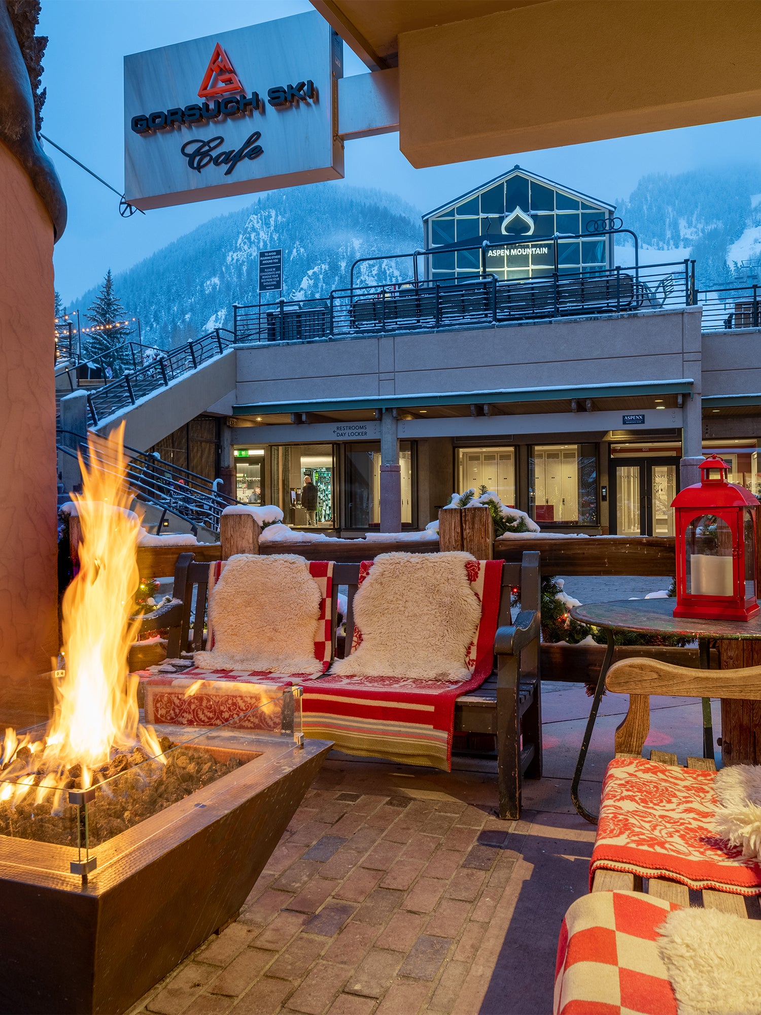 Outside patio with benches and a fire pit with Gorsuch Ski Cafe sign above and Aspen Mountain in the background.