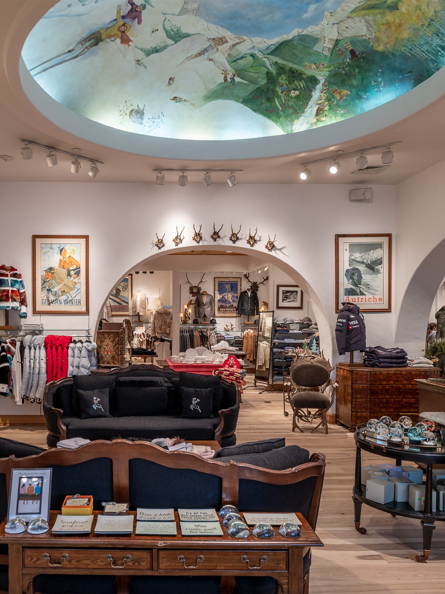 Interior of the Gorsuch Beaver Creek store with skier painting on the ceiling and clothing and furniture on the selling floor.