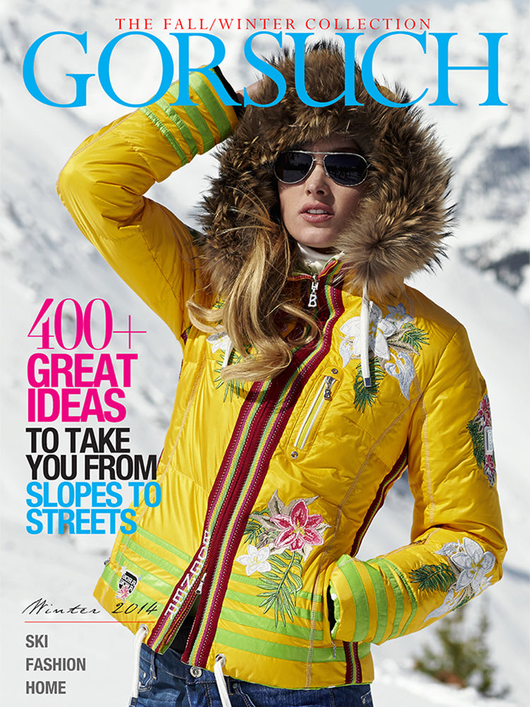 2014 Gorsuch catalog cover with a woman in bright yellow ski jacket with flowers on it, fur trim hood on her head and snowy mountains in the background.