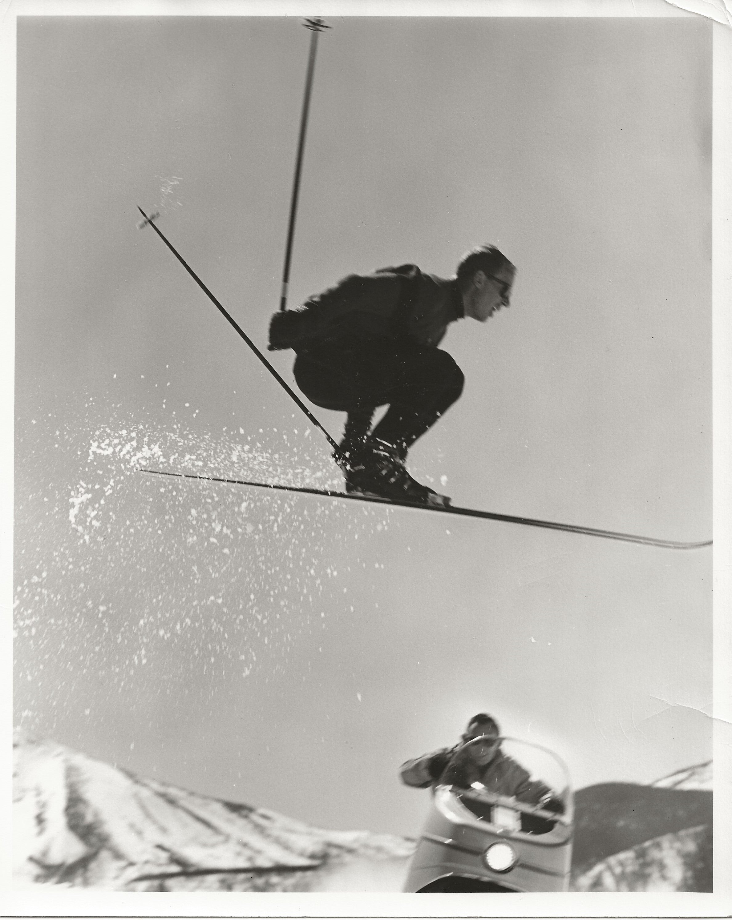 David Gorsuch skiing in the snow with a snowmobile in the background.