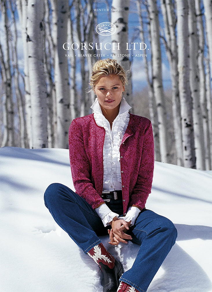 2003 Gorsuch catalog cover with women in white ruffled shirt and pink cardigan sitting in the snow with aspen trees in the background.