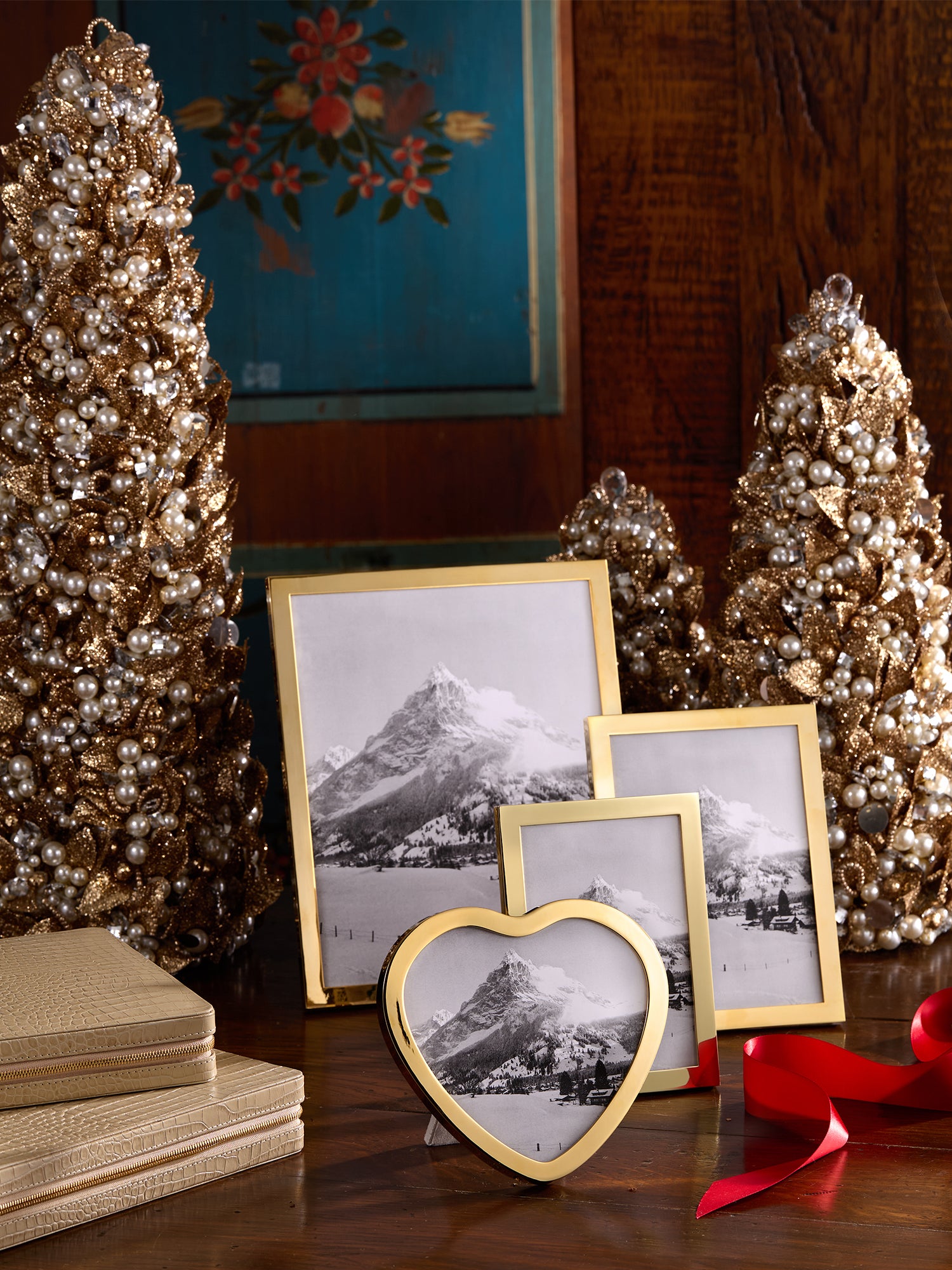 Decorative gold frames, small Christmas trees, and a red ribbon arranged on a wooden surface.