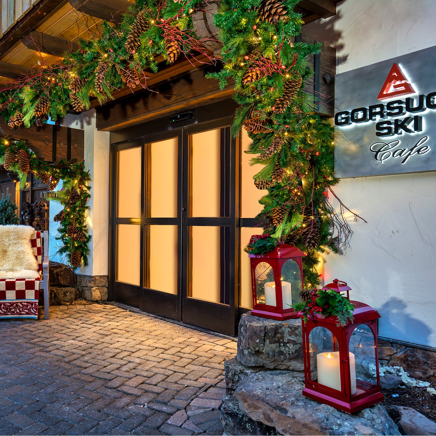 storefront of Gorsuch Ski Cafe in Vail with branded sign and garland with pinecones and red lanterns decorated for the holiday season.