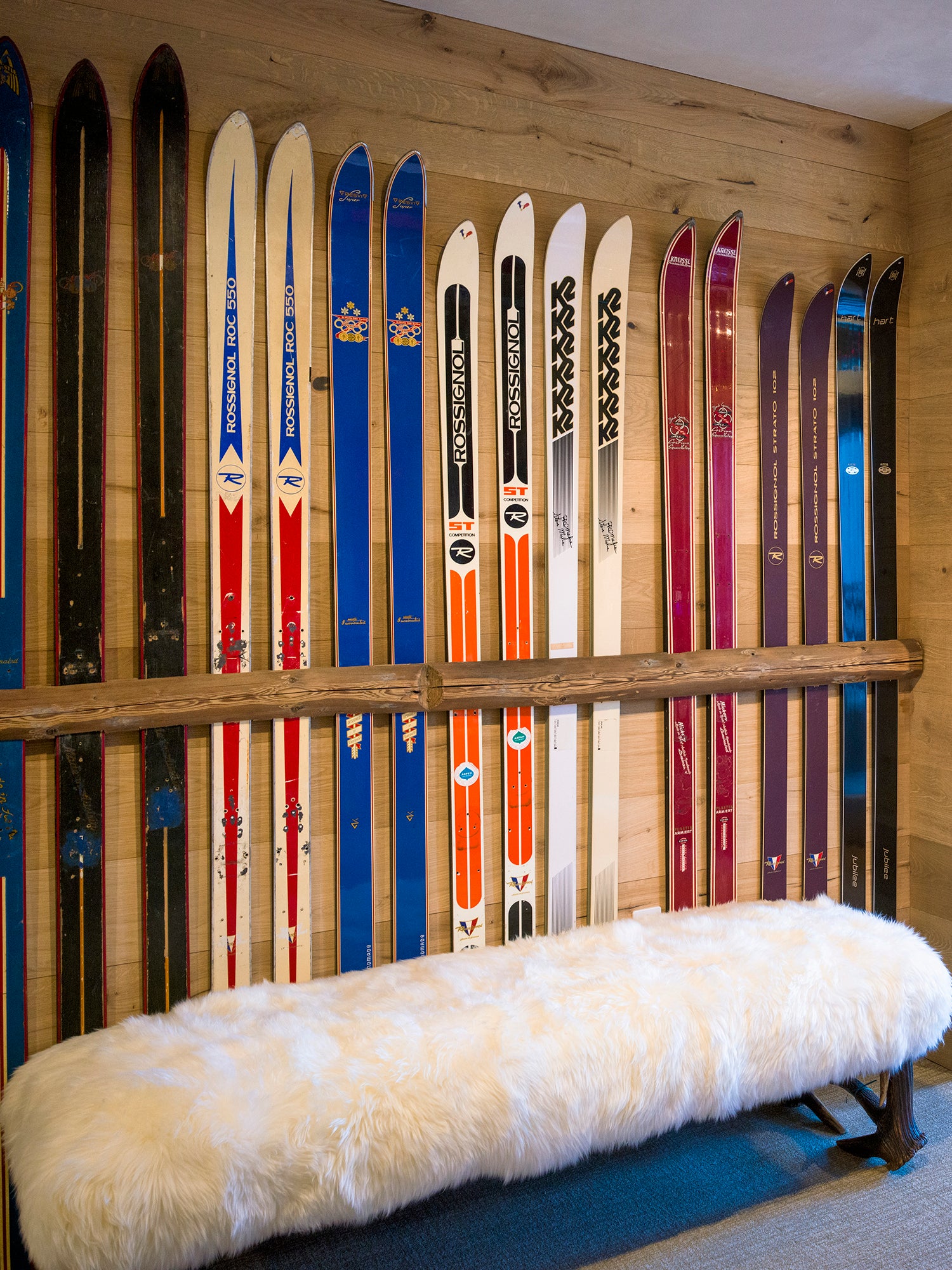 Collection of vintage skis displayed on a wooden wall with a bench in the foreground.