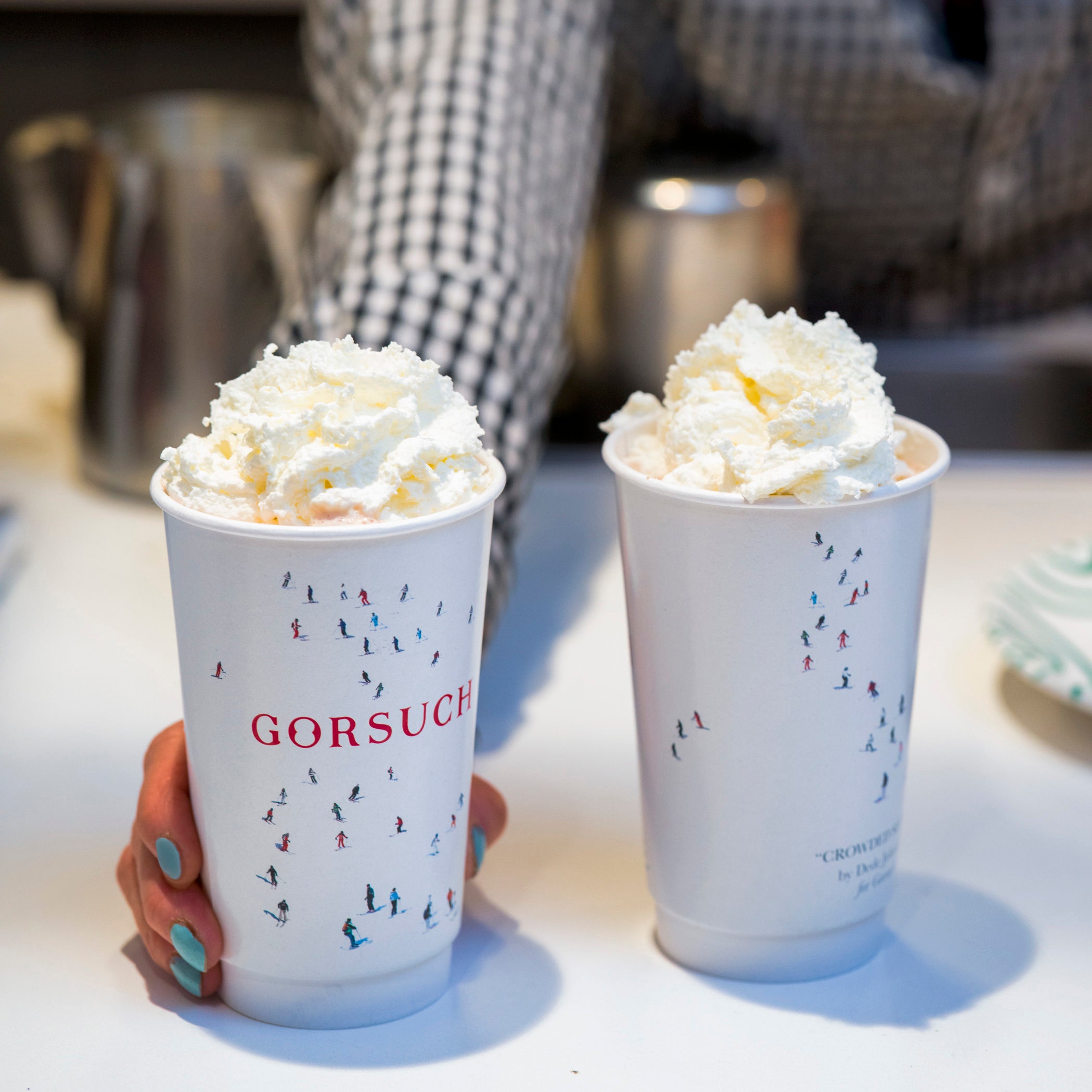 Two cups of hot chocolate with whipped cream, branded 'GORSUCH', on a table.