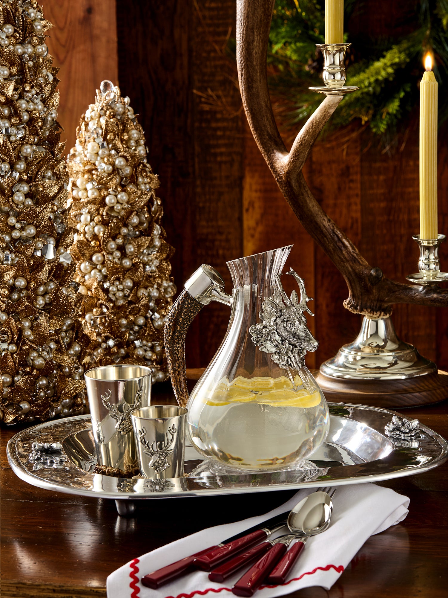 Decorative setting with a glass carafe, silver tray, and Christmas trees.