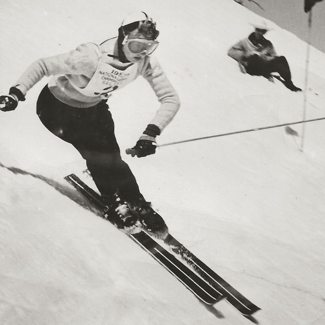 Vintage image of Renie Gorsuch skiing downhill in a race, wearing a sweater, goggles, and a helmet.