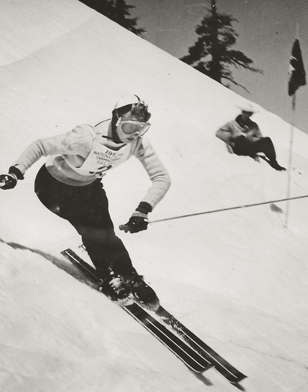 Vintage image of Renie Gorsuch ski racing in an event wearing a sweater, goggles and a helmet.
