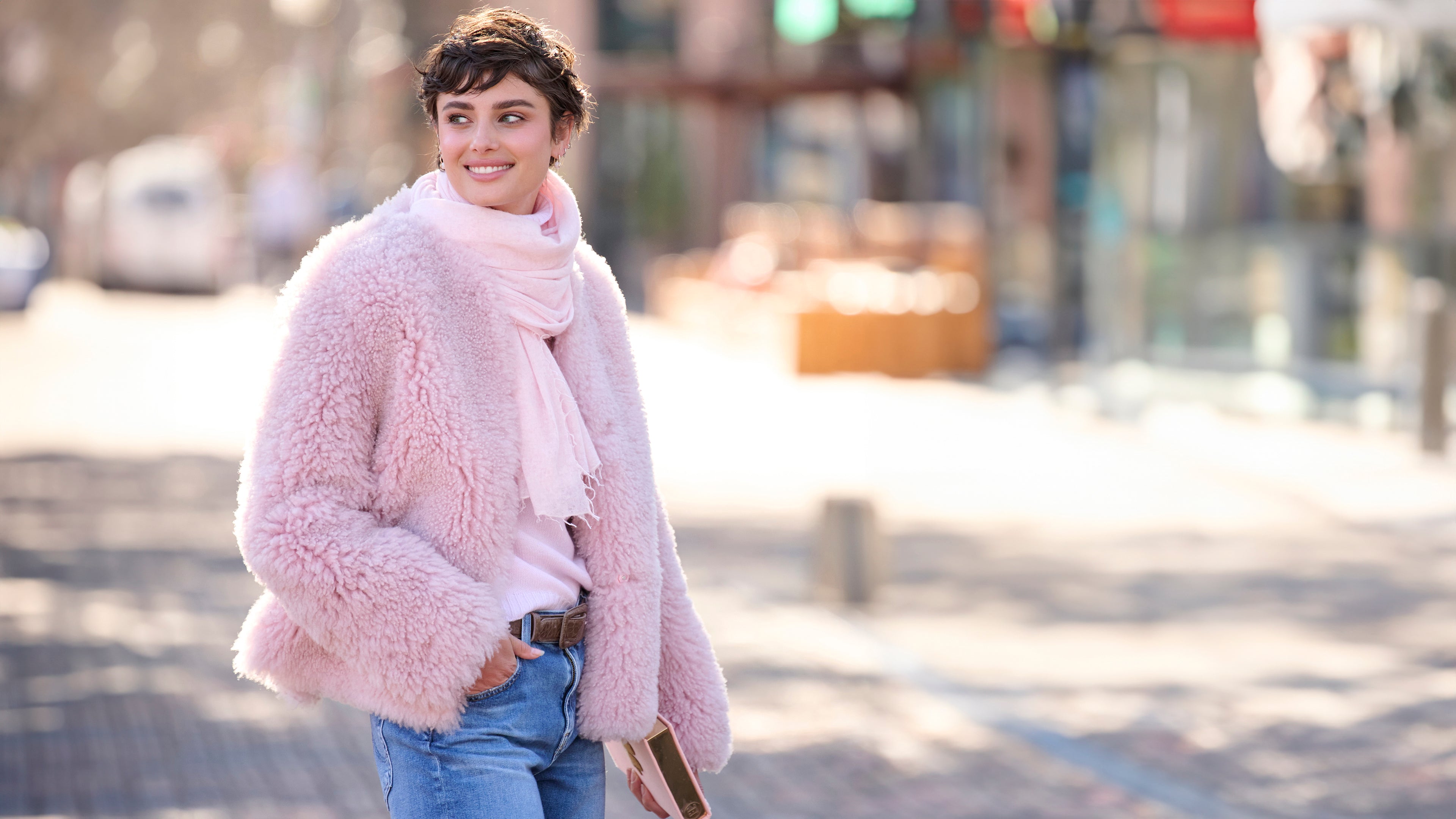 Woman wearing a pink fluffy coat and scarf on a city street.