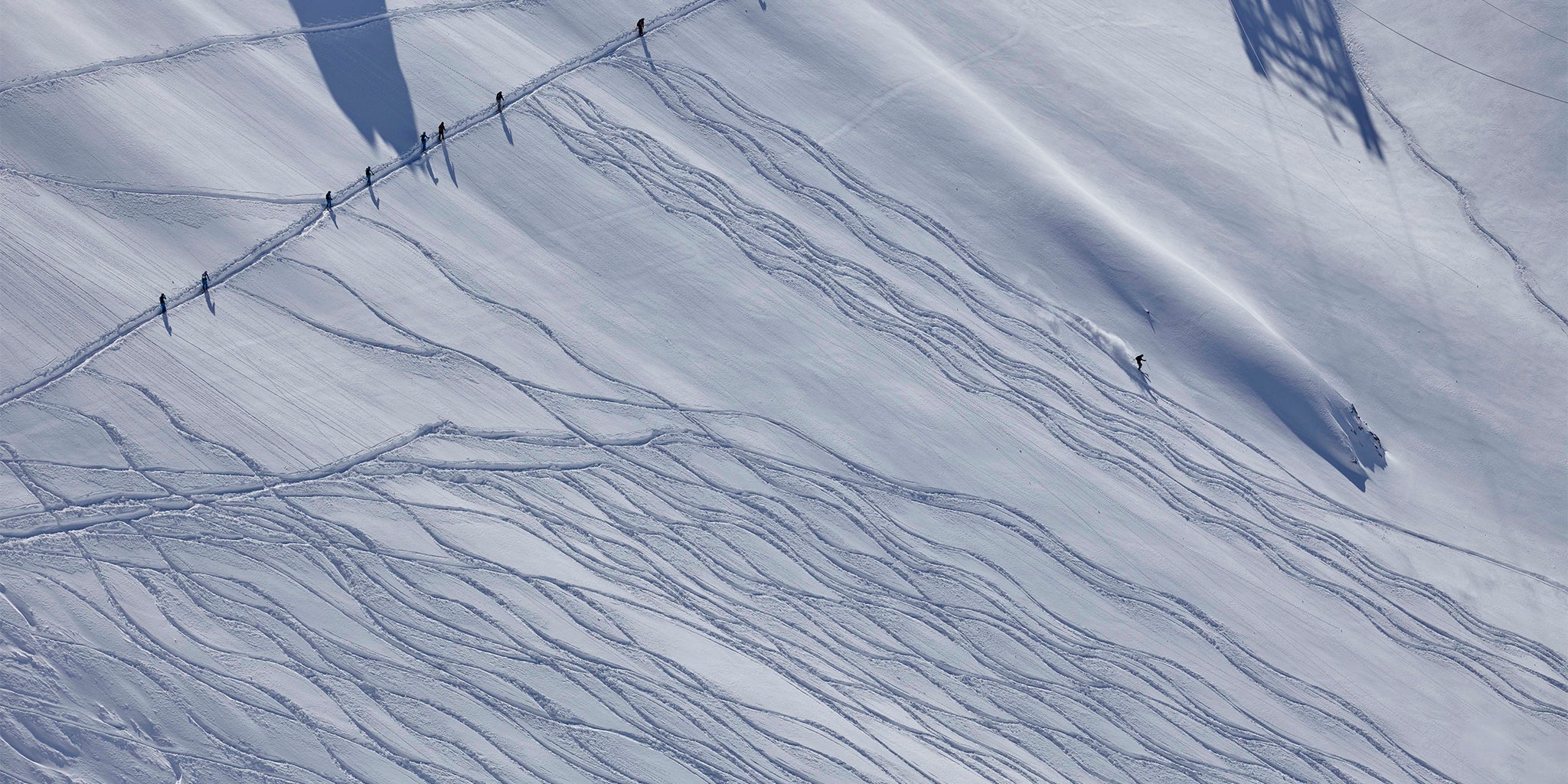 skiers descending a snowy mountain slope with tracks in the snow.