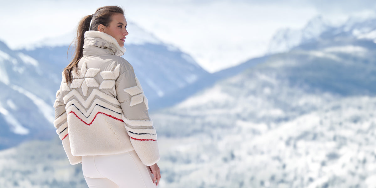Woman wearing the Bogner Felia Down Ski Jacket in Dune with a Norwegian pattern, standing in a snowy mountain landscape.