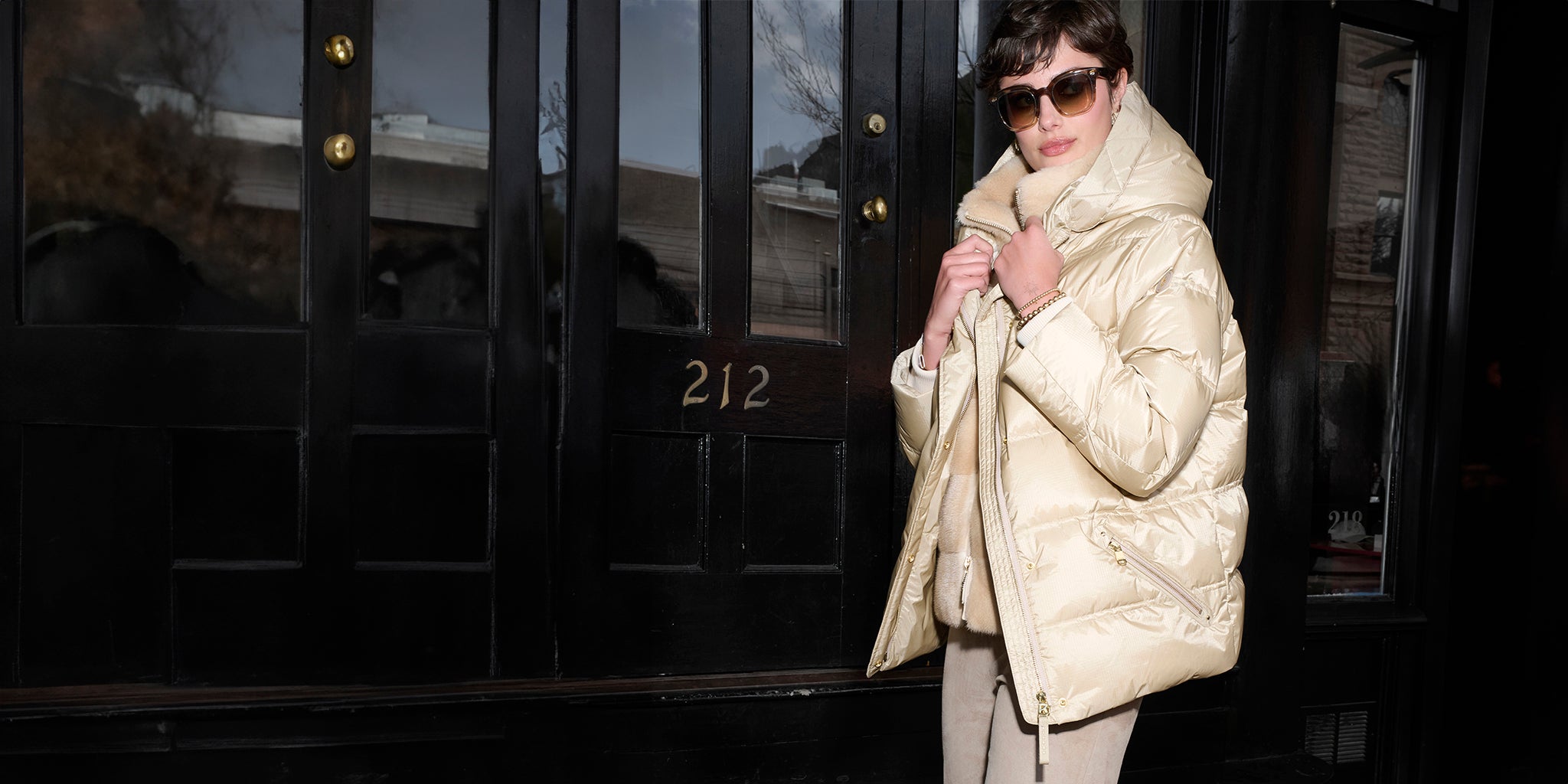 Person wearing a cream puffer coat standing in front of a door with the number 212.