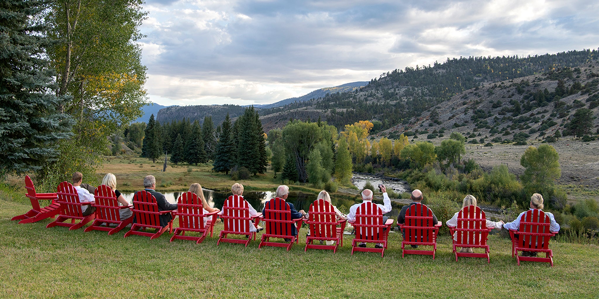 Gorsuch family sitting on red chairs in a scenic outdoor setting with mountains and trees.