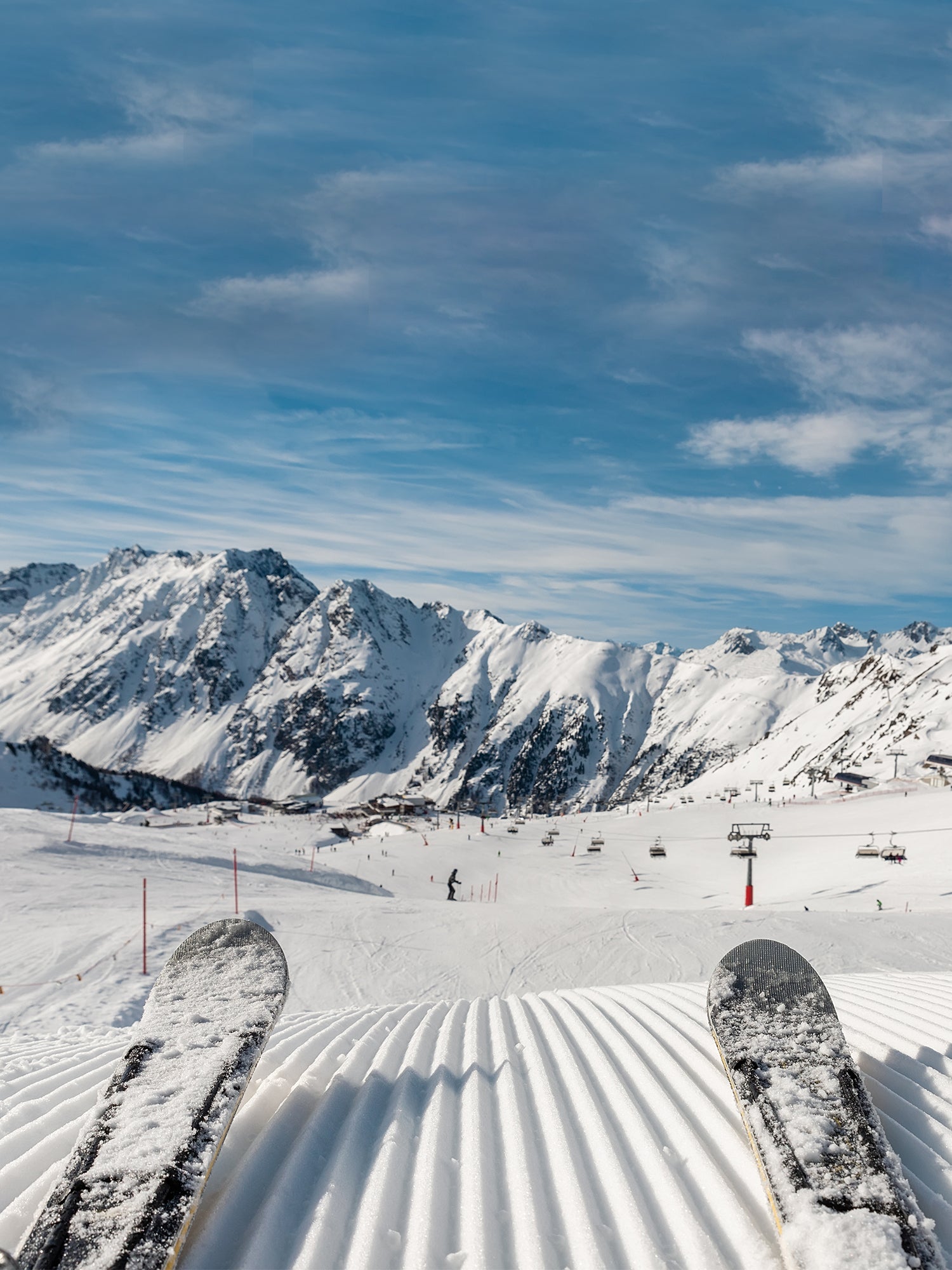 Two skis on top of freshly groomed snow with mountains and chairlift in the background.