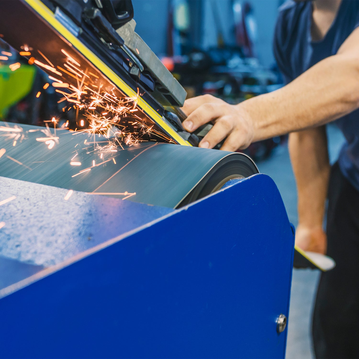 Man with pair of skis in his hand and grinding the bottom of the skis over a machine.